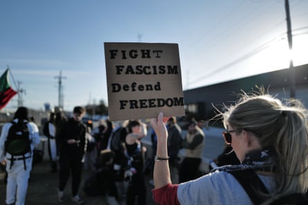 a person holds a sign that reads ‘fight fascism defend democracy’