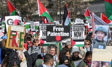 A group of protesters holding Palestinian flags and placards bearing words such as 'Free Palestine' and 'Ceasefire now'.