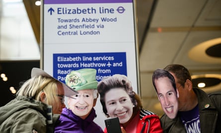 Rail enthusiasts wearing royal masks take a selfie in front of an Elizabeth line sign.
