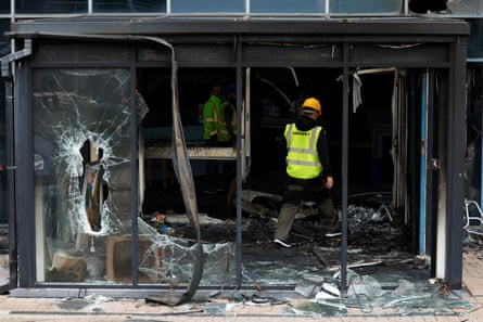 Man in a hi-vis jacket walks through a shop front with its glass windows completely bashed in