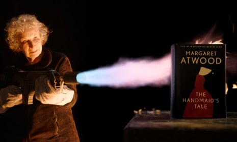 Author Margaret Atwood using a flamethrower near an unburnable copy of The Handmaid's Tale. 
