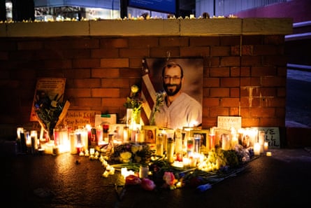 a picture of a man leans against a low brick wall as candles and flowers are arranged around it