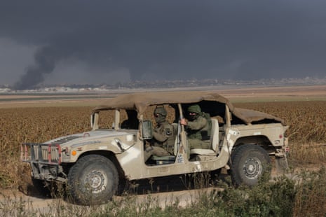 An Israeli military vehicle drives past billowing smoke in the distance at the border with the Gaza Strip