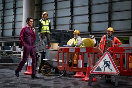 Sacha Baron Cohen walks past some workmen in a street
