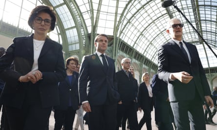 France’s president flanked by officials with the glass and steel vaulted roof of the venue behind them