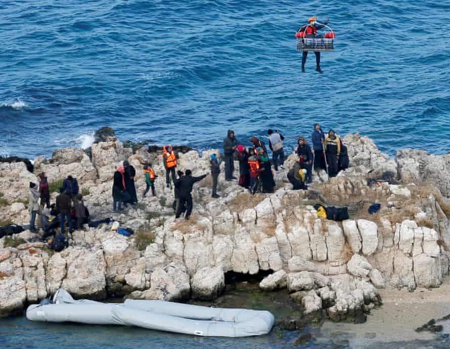 A Turkish coastguard crew member hangs on a rope attached to a helicopter above some rocks near İzmir.