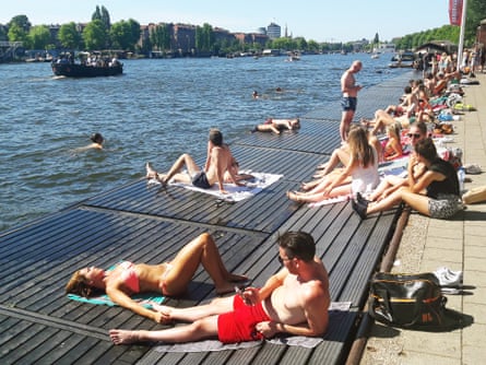 Large crowd of people sunbathing on a wooden pier on the Amstel River