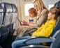 A woman shows a tablet to a boy and girl in airline seats