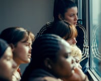 Several women lean close together, gazing out a train window with pensive expressions in 15/18 A Place to Heal.
