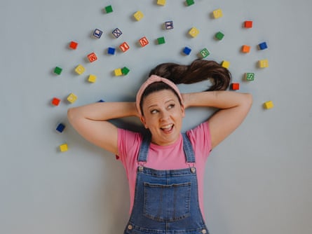 Ms Rachel lying down wearing dungarees and surrounded by children’s coloured blocks