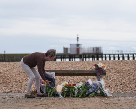 A woman lays flowers in memory of the three family members on the beach at Shoreham-by-Sea