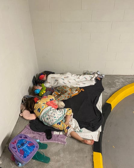 Children asleep on a blanket on a kerbed area in the corner of the car park