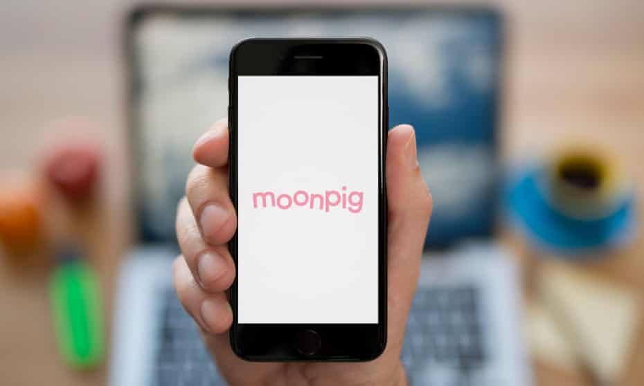 A man looks at his iPhone which displays the Moonpig logo