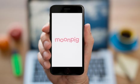 A man looks at his iPhone which displays the Moonpig logo