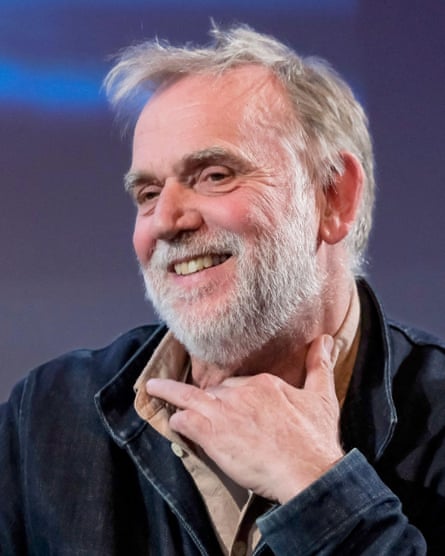 A head-and-shoulders portrait of a man with greying mousey hair and a grey beard smiles widely
