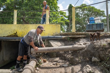 A man stand by a roadside next to a large damaged pipe surrounded by rubble