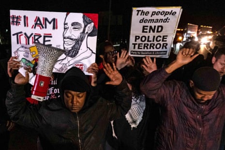 People stand on a road with their arms raised above their heads. A sign reads 'The people demand: End police terror'.