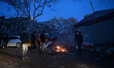 People stand at a bonfire bonfire among the rubble of collapsed buildings in Kahramanmaras, on 7 February 2023.