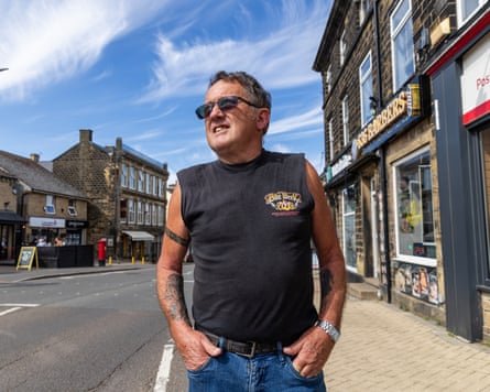 Richard Riding in a short-sleeved T-shirt with his hands in his pockets. He is standing on a high street on a sunny day.