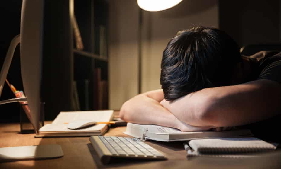 Exhausted overworked young man studying and sleeping on the table in dark room at home
