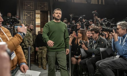 Volodymyr Zelenskiy walks past members of the press holding up cameras