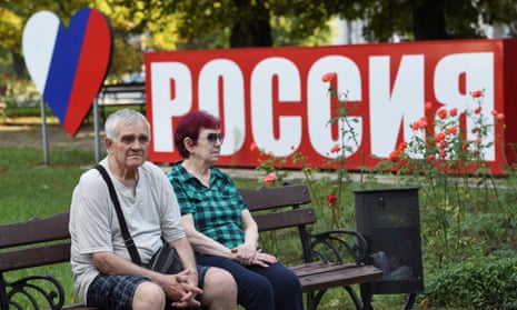 An elderly couple sit on a bench next to a board that reads ‘Russia’ in central Donetsk
