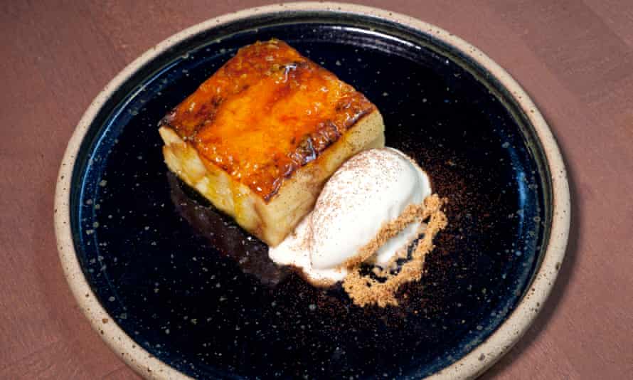 A square of bread and butter pudding with a caramelised top and a scoop of ice-cream next to it on a round dark blue plate