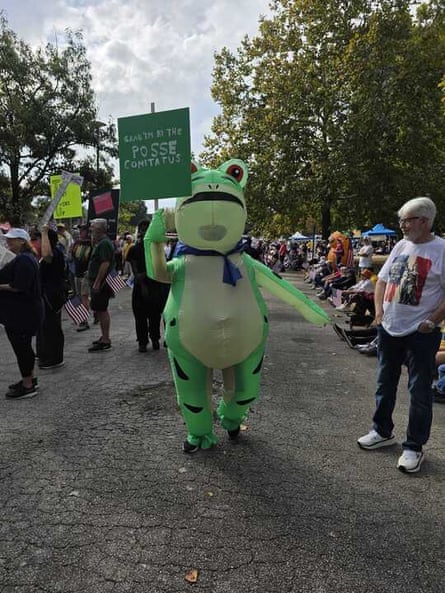 man in inflatable frog suit stands outside and holds a sign about ‘the posse comitatus’