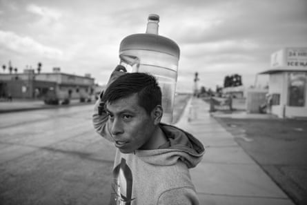 A man in a hooding holding a full jug of water on his shoulder