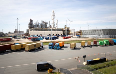 Parked lorries and trailers, with large buildings and wind turbines in the distance