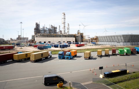 Parked lorries and trailers, with large buildings and wind turbines in the distance