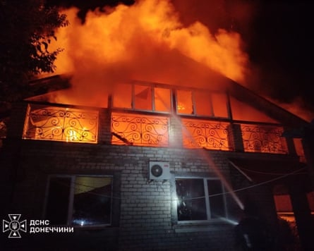 A warehouse on fire as a firefighter works to put it out.