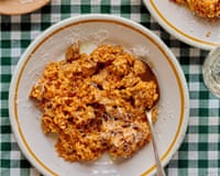 Two plates of Sardinian rice with pork and saffron, with cutlery and a plate of grated pecorino on a chequered tablecloth.