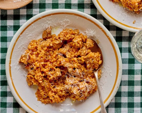 Two plates of Sardinian rice with pork and saffron, with cutlery and a plate of grated pecorino on a chequered tablecloth.