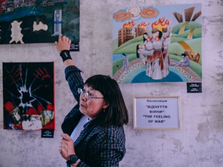 An older woman with a black bob points to a painting while talking to someone off-camera