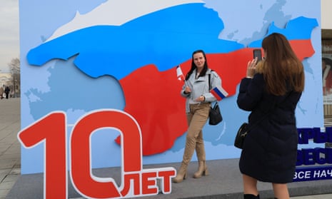 A woman poses for pictures with an art decoration featuring the map of Crimea in the colours of the Russian flag.