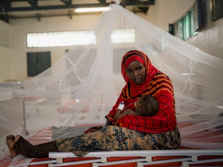 A Somali woman cradles her 14-month-old baby on a hospital bed under mosquito netting