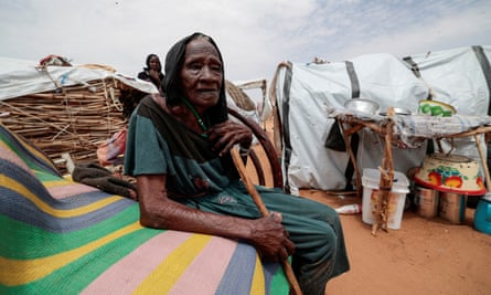 Halima Haroun Mohammed, 115, a Sudanese woman who fled the conflict in Geneina, sits outside her temporary shelter while holding a walking stick