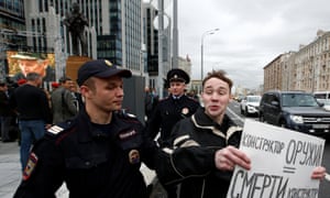 A man is detained by police as he holds a sign reading, ‘a creator of weapons is a creator of death’.