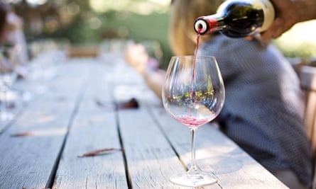 A glass of red wine is poured, on an outdoor table in green surroundings.