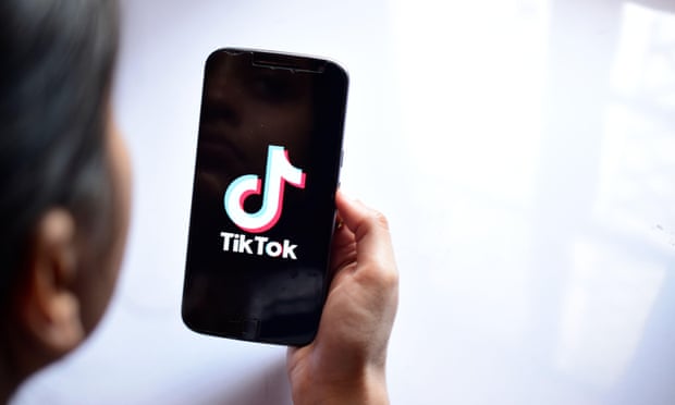 A woman holding a phone with the TikTok app