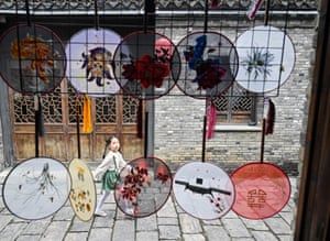 A young girl can be seen walking down a stone road as round, translucent fans hang in the foreground