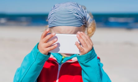 A child holds a mobile phone at a beach