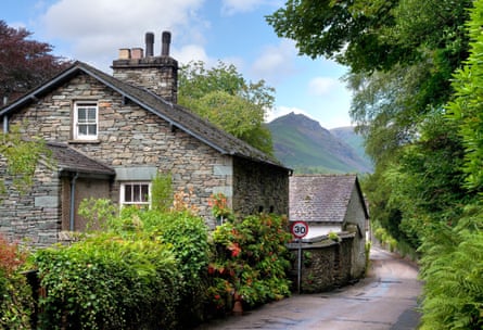 A stone house with multi-paned windows and a pretty garden, with mountains in the background