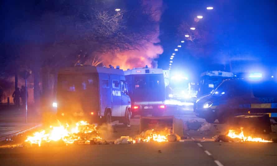 Se ven camionetas de control de disturbios de la policía cerca de contenedores de basura en llamas después de una manifestación organizada por Rasmus Paludan en Malmo.