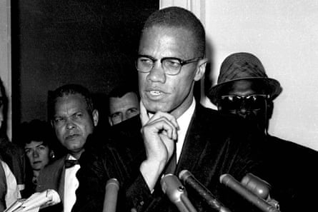 black and white photo of man in suit and glasses speaking into microphones