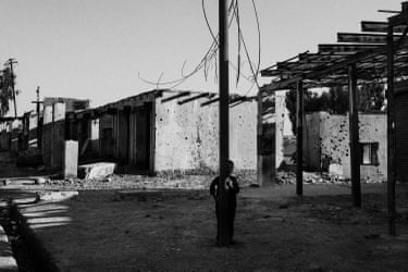 A child standing behind a telegraph pole amid damaged buildings