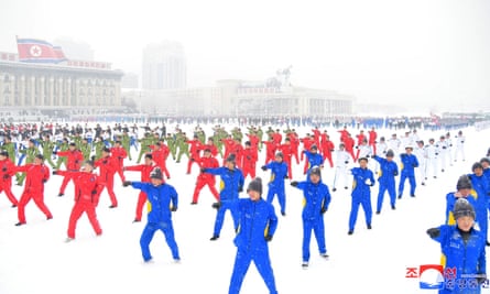 People arranged in neat rows wearing red and blue jumpsuits perform a choreographed dance