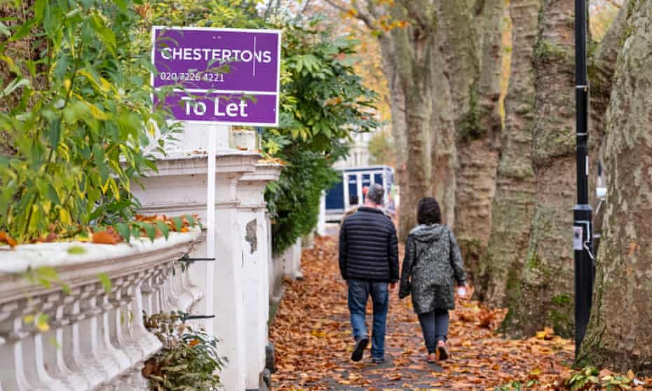 Couple walking down leafy street with estate agent sign