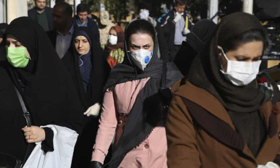 People wearing face masks walk on a sidewalk in downtown Tehran, Iran